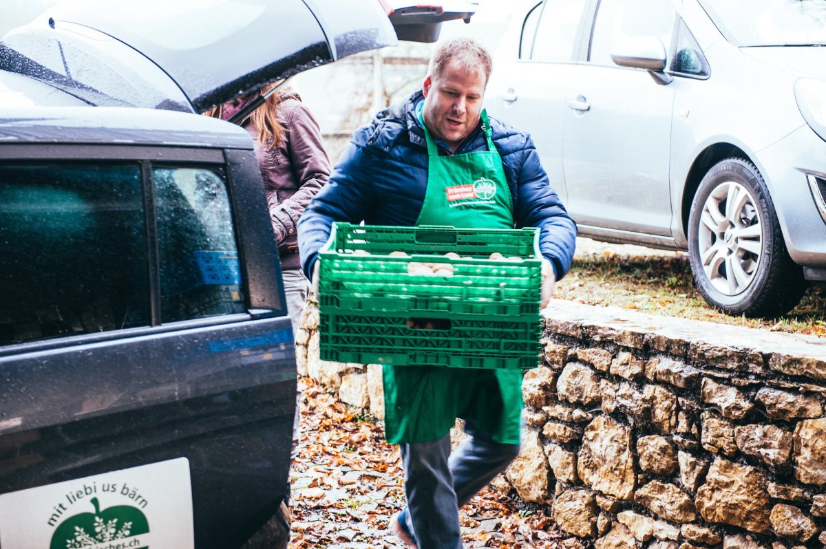 Mitarbeiter von Frisches.ch trägt eine grüne Lieferkiste aus dem Fahrzeug